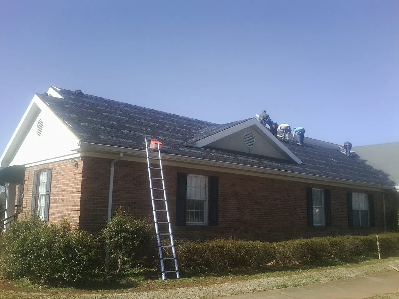 Crew tearing shingles off a brick ranch roof with a ladder set — Metal Roof Repair work by our crew in Lakewood