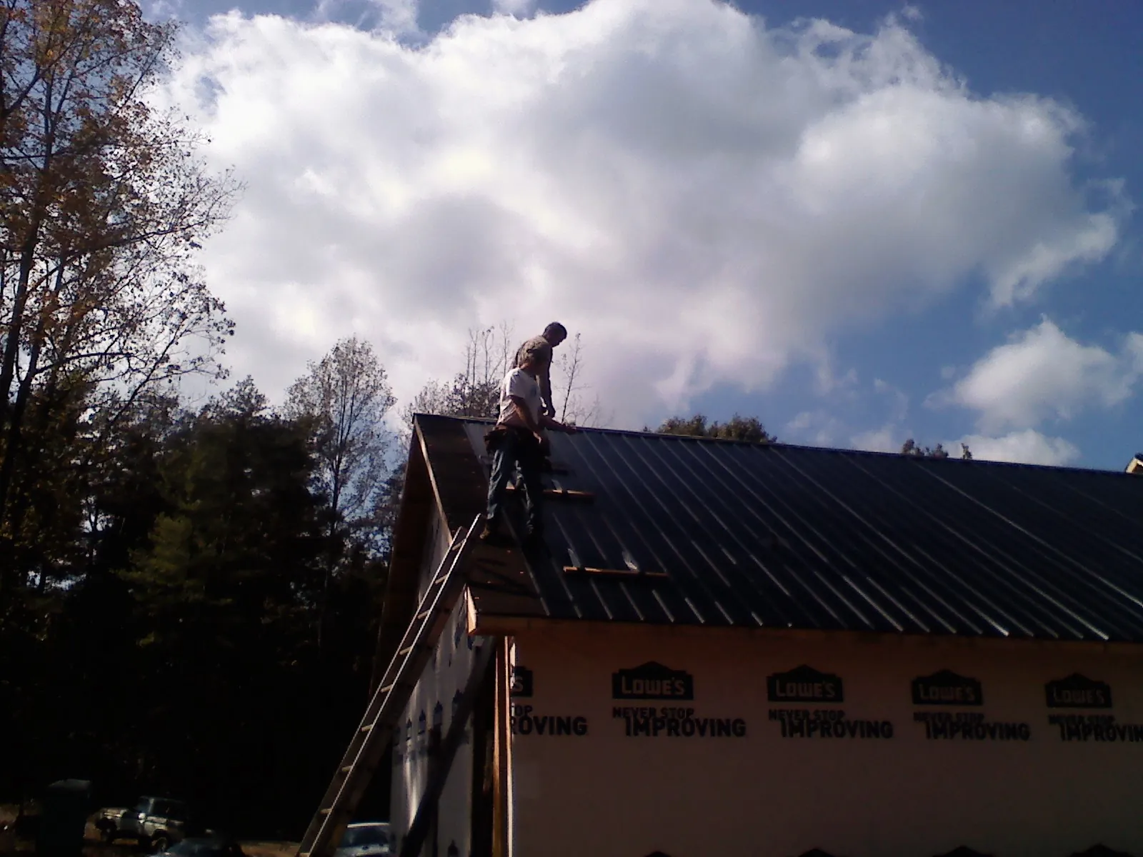 Roofer fastening dark metal panels high against a cloudy sky, from a Roof Inspection job in Lakewood